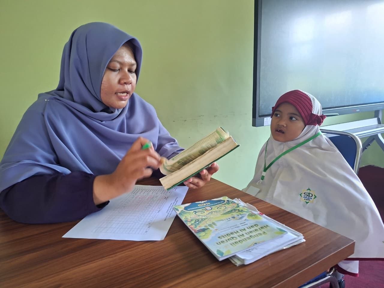 Ustadzah memverifikasi capaian hafalan melalui buku Pengendali Hafalan Al-Quran dan Hadits